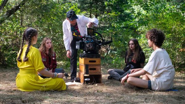 On a movie set, a person stands over a camera while working with four people sitting on the ground.