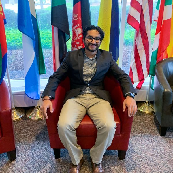 Dilli Gautam sits in a chair in front of seven country flags