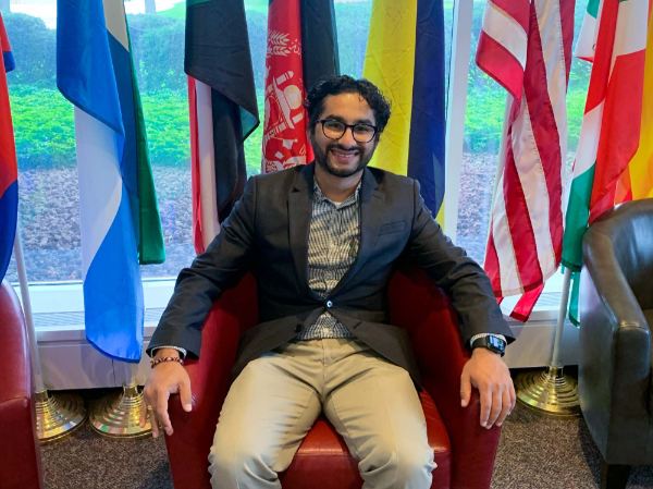 Dilli Gautam sits in a chair in front of seven country flags