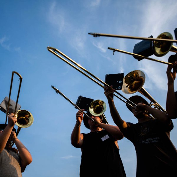 A group of people playing trombones is seen from ground level.