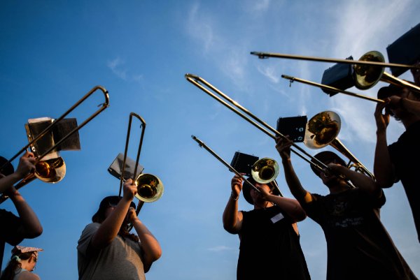 A group of people playing trombone are seen from ground level.