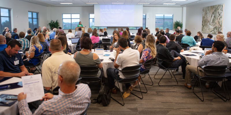 woman at podium before large group of people seated at tables