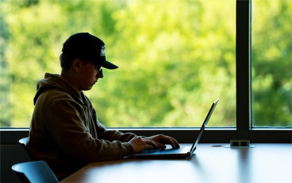 A student wearing a hat uses a laptop. 