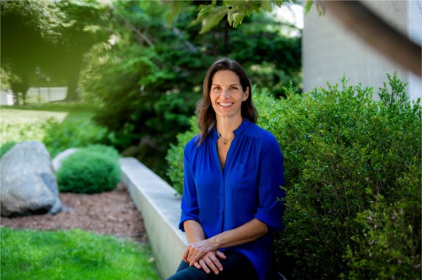Jennifer Moore in blue shirt seated on outdoor wall outside Zumberge Hall