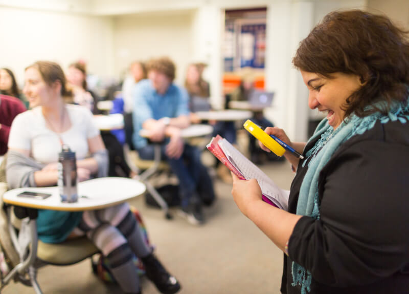 Professor looks through magnifying class in front of classroom.