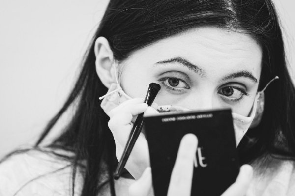 Actor putting on makeup while wearing a mask