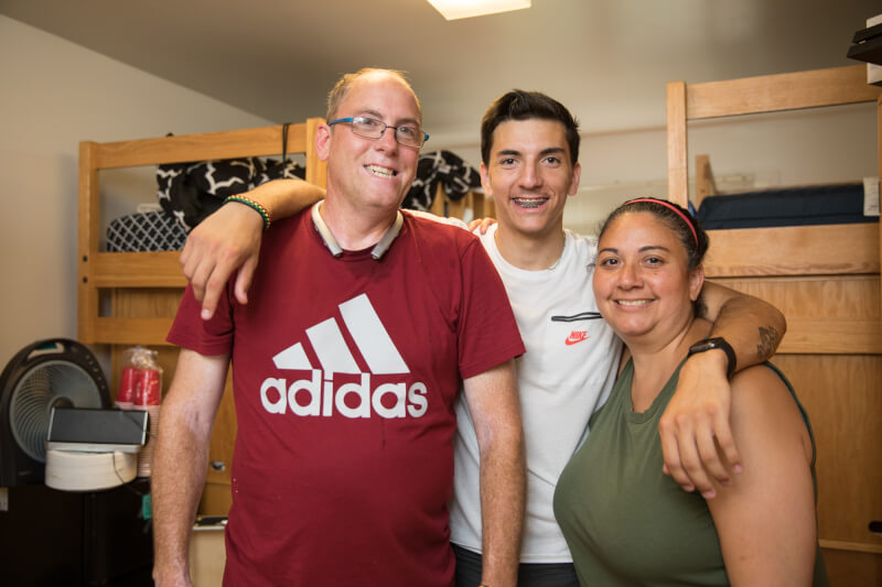  Mother, father, and son hugging in dorm room