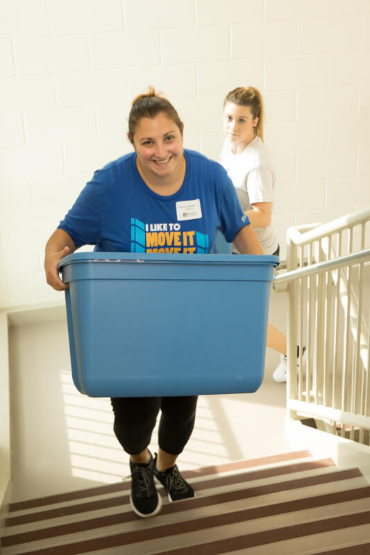  GVSU Alumni carrying blue crate up stairs