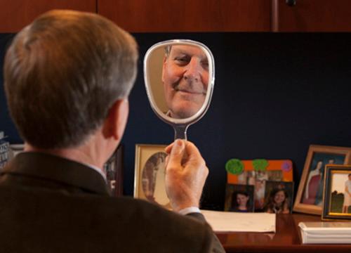 President Thomas J. Haas checks himself, sans mustache, in the mirror. He and other West Michigan leaders are in a contest to grow mustaches during November to raise awareness for men's health.