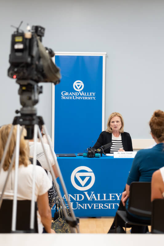 woman seated at table, media camera videotaping her