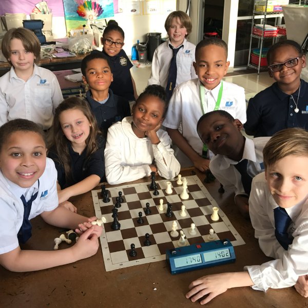 Students' chess club pose around chessboard