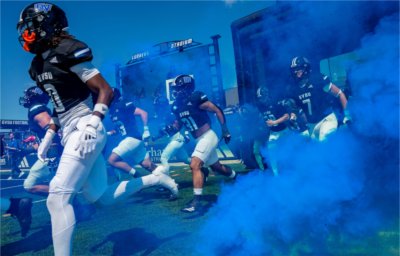Grand Valley football players run on to the field at Lubbers Stadium through a cloud of blue smoke.