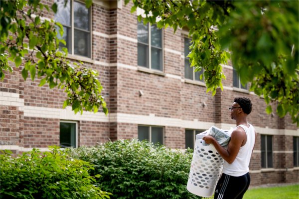 A student carries a laundry basket full of his clothes into a living center.