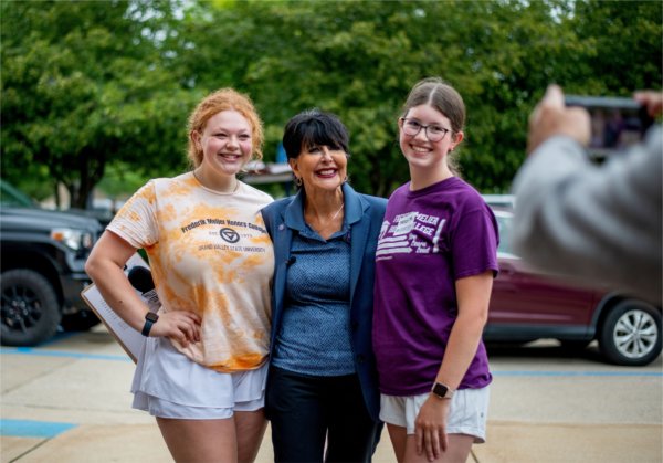 Three people stand with their arms around each other and smiling during move-in at GVSU.