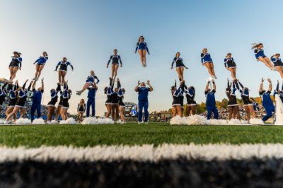  A line of cheerleaders on the sidelines of a football field are tossed into the air.