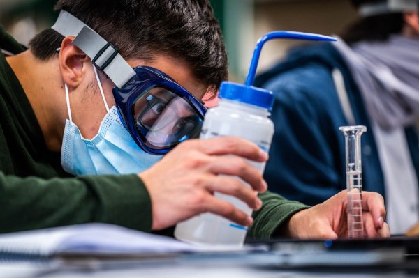  A person wearing goggles looks at and holds a beaker