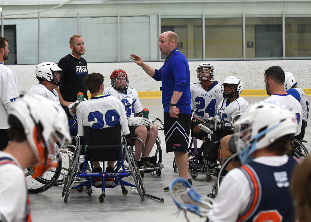 coach standing in center of wheelchair lacrosse athletes