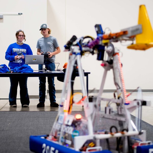 two people stand at a table, a robot from FIRST Robotics in the foreground