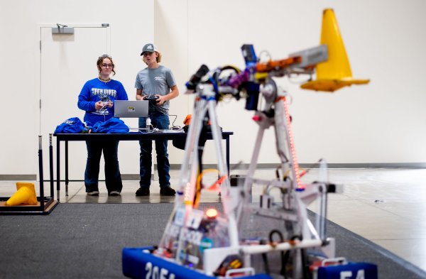 two people stand at table, robot from FIRST Robotics in the foreground