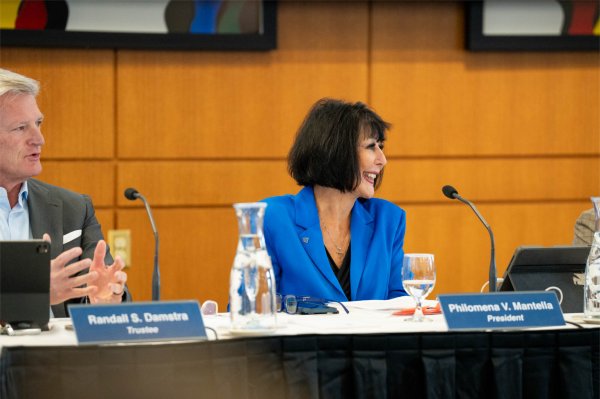 A person smiles while looking off to the side. The person is seated at a table.