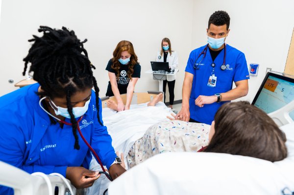 Physician assistant, nursing and occupational therapy students work in a sim lab with a mannequin.