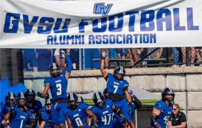 Grand Valley football run underneath a banner before the start of a game.
