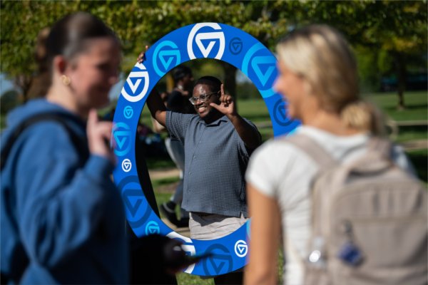 A person gives the anchor up sign while posing for a photo in a circular shape showing the GV logo. 