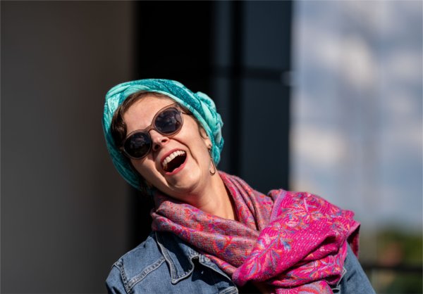 A person wearing brightly-colored scarves laughs.