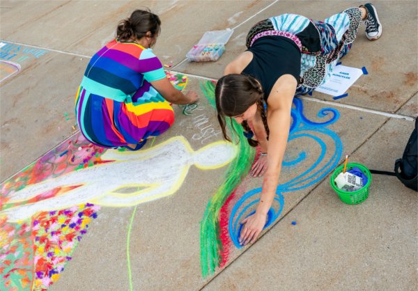 College students work on colorful sidewalk chalk drawings. 