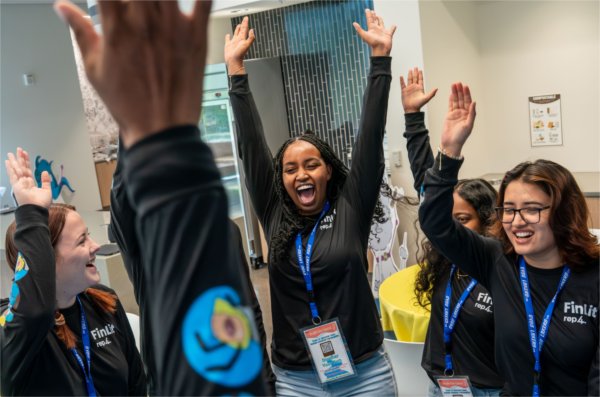 A group of students with happy faces raise their hands in the air. 
