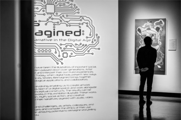 A silhouetted person looks at a piece of art on the wall. Text can be seen on a wall in the right foreground.