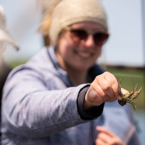 A student in sunglasses holds a crayfish while on a schooner, some species of crayfish are invasive to the waters in northern Michigan.