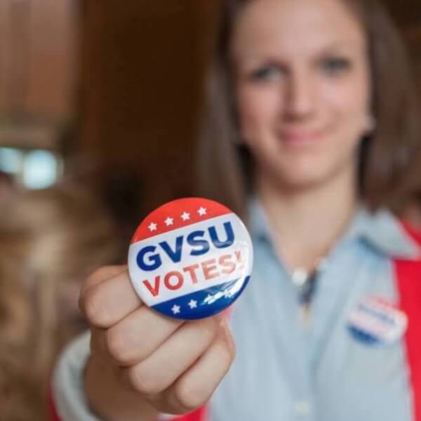 A photo of a student holding up a GVSU Votes! button.