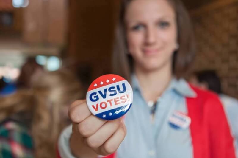 A photo of a student holding up a GVSU Votes! button.