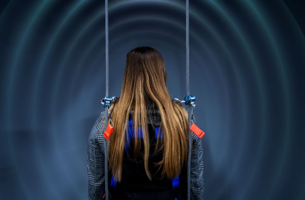  The back of a person with long hair, inside a device. They are attached to it with ropes from above and there are circles expanding out around the person.out