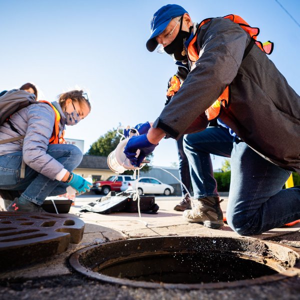 Researchers retrieve a water sample through a hole in the street used for maintenance.