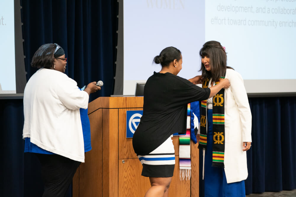 Takeelia Garrett and Nikki Gaines from the Black Faculty and Staff Association present President Mantella with a kente stole.