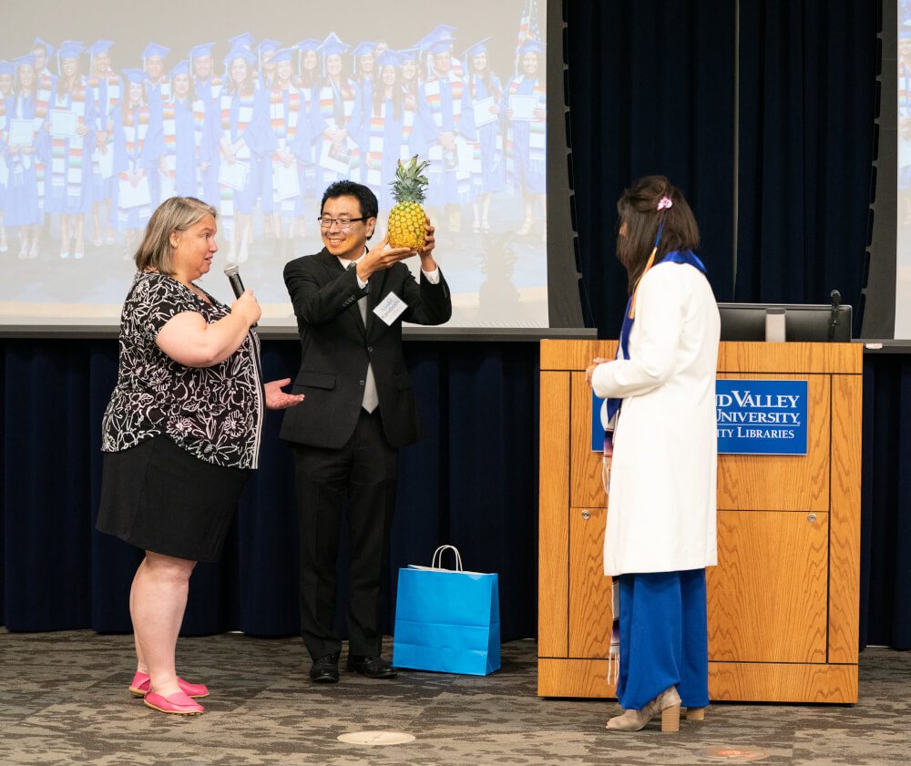 Kate Stoetzner and Naoki Kanaboshi with International Faculty and Friends present President Mantella with a pineapple, an international sign of hospitality.