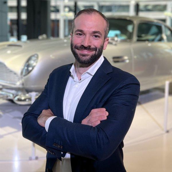 Jeff Rogg poses for a portrait in front of an Aston Martin DB5.