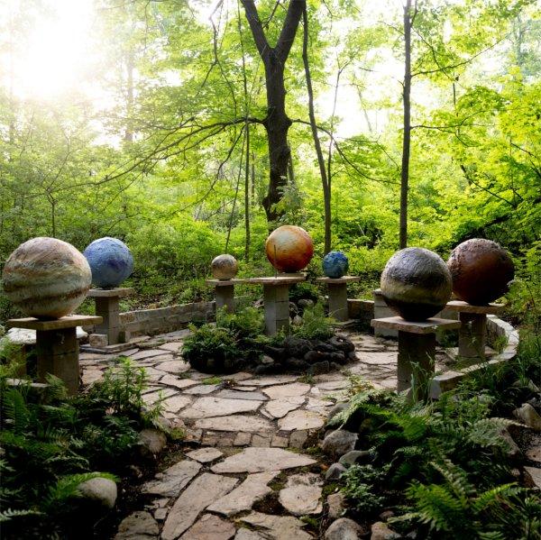 An outdoor stone sculptural garden depicting planets, with greenery around it.