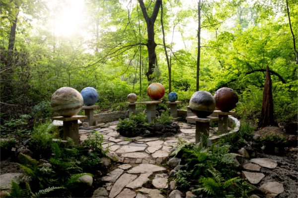 An outdoor stone sculptural garden depicting planets, with greenery around it.
