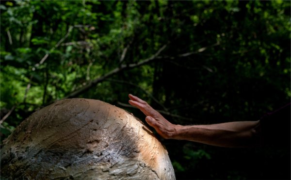 A person places a hand on a stone planet sculpture. 