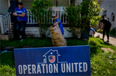 yard of home with porch in background, yard sign Operation United in blue in front