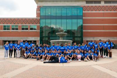 large group of students, faculty and staff members dressed in blue t-shirts and posing in front of the Student Services Building fountain