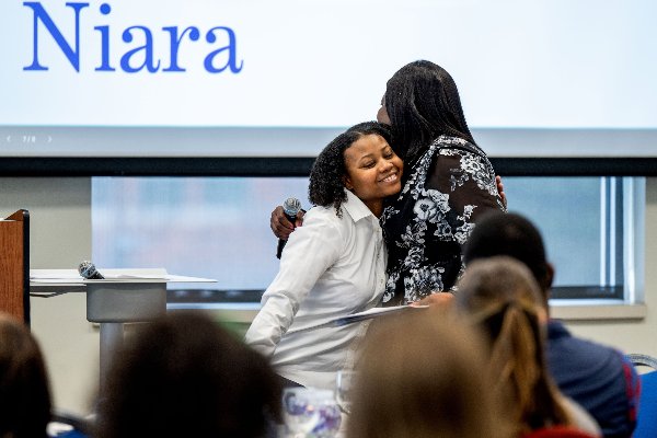 A student in a white blouse is hugged by keynote speaker Ronke Olawale after introducing her to speak. 