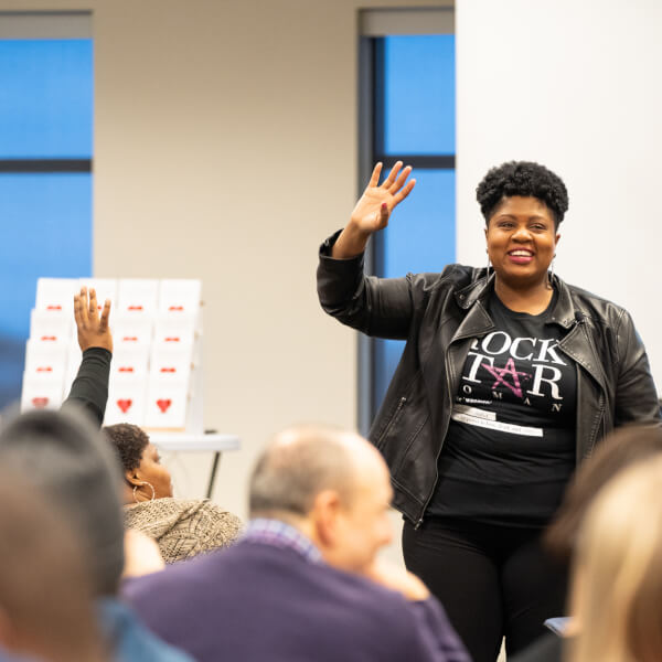 woman at front of room with arm raised