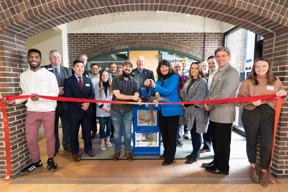 Grand Valley Lanthorn staff, President Philomena V. Mantella and community members celebrate the newspaper's 100th distribution site at a ribbon-cutting ceremony in Kirkhof Center on the Allendale Campus January 31.