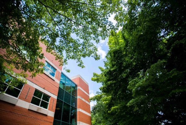 Padnos Hall is pictured behind a foreground of green trees and a bright blue sky