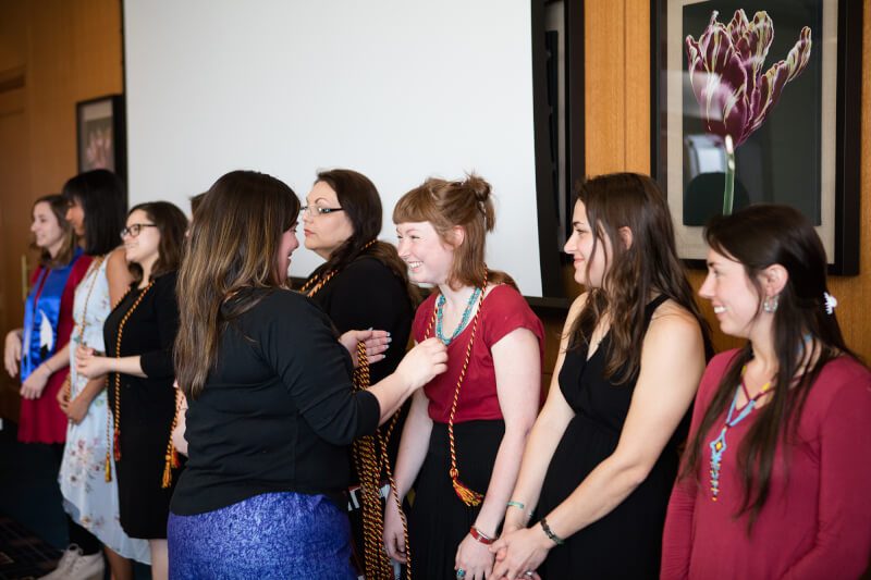 group of women, one presenting graduation cords
