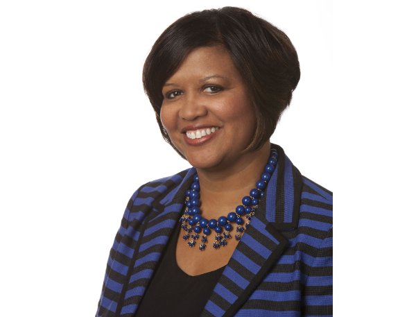 Tia Brown McNair in a seated portrait wearing a blue and black striped jacket with a blue beaded necklace